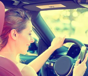 A woman is driving and looking at her phone at the same time