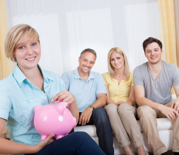 two girls and two boys are sitting on a couch holding a piggy box